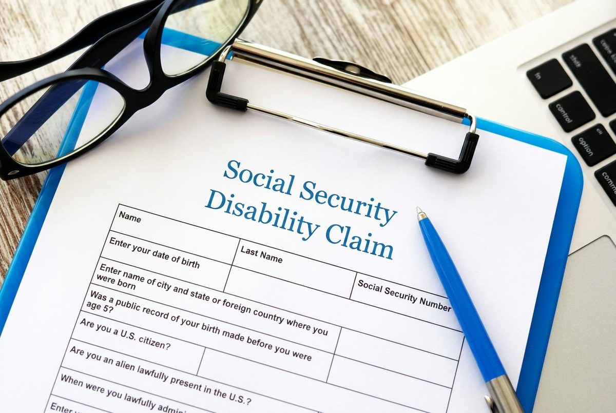 Social Security disability claim form on a clipboard with reading glasses and a pen